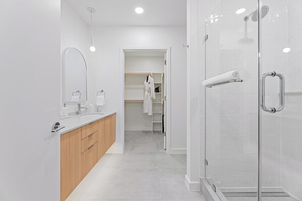 A modern bathroom with a glass shower enclosure, a wooden vanity, and a walk-in closet. - Steps from Zilker & Lady Bird | Private Balcony + Pool, Terrace, Dining, Bar (Austin)
