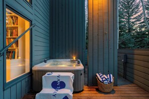 Eine Holzterrasse mit Whirlpool, einer Bücherablage und einem Wäschekorb mit Handtüchern.