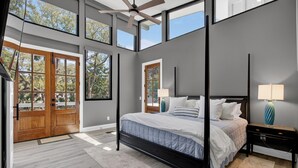 A bedroom with a large bed, two bedside tables, a ceiling fan, and large windows. - Private Pool + Outdoor Lounge + Movie Room + Game Room | Summerset by AvantStay (Isle Of Palms)