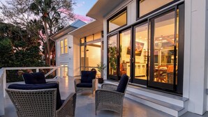 A covered outdoor seating area with wicker chairs and a view of the interior through large glass doors. - Private Pool + Outdoor Lounge + Movie Room + Game Room | Summerset by AvantStay (Isle Of Palms)