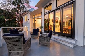 A covered outdoor seating area with wicker chairs and a view of the interior through large glass doors.
