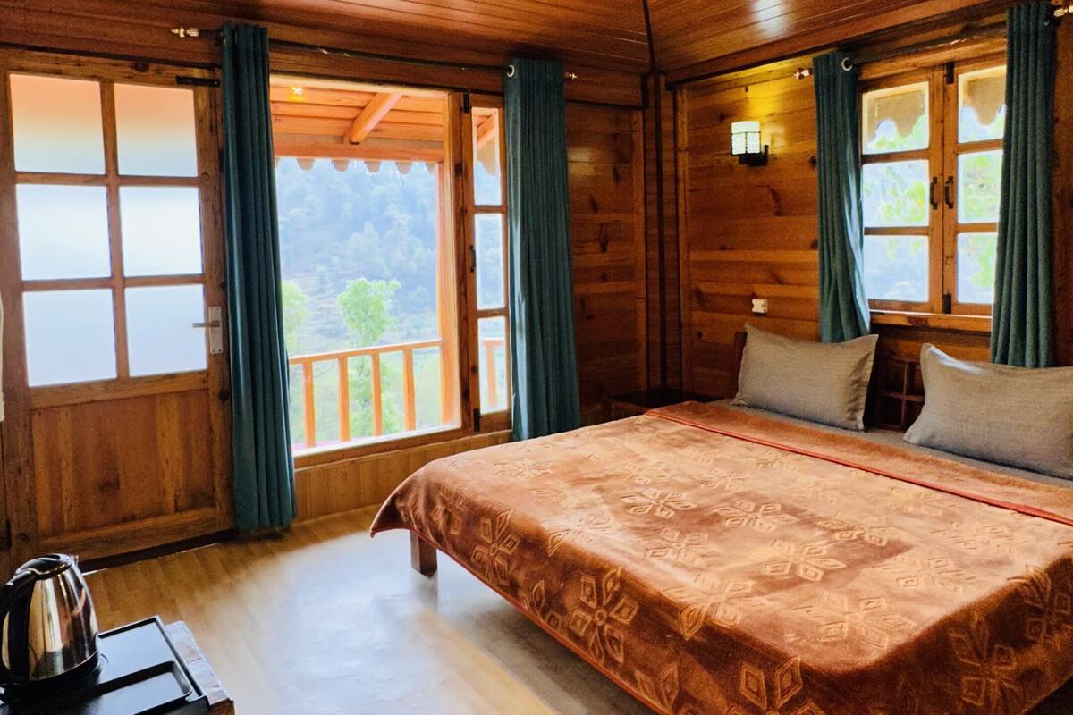 Une chambre dans un chalet en bois, avec un lit, une table et une bouilloire, et une vue sur l’extérieur.