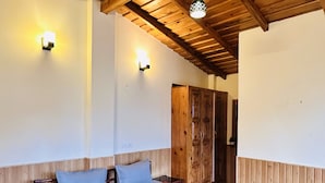 Ein Zimmer mit Holzboden, einem Bett mit roter Decke, zwei Wandleuchten und einem Holzschrank.