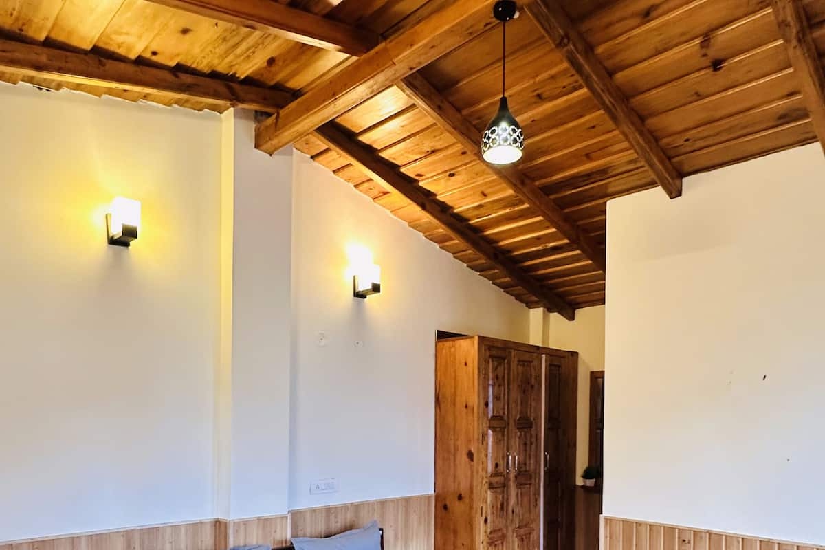Une pièce avec un plafond en bois, un lit recouvert d’une couverture rouge, deux lampes fixées au mur et une armoire en bois.