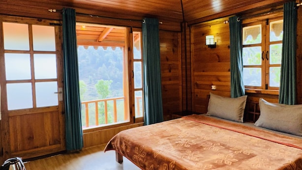 Ein Holzhütten-Zimmer mit Bett, Tisch mit Wasserkocher und Blick ins Freie.