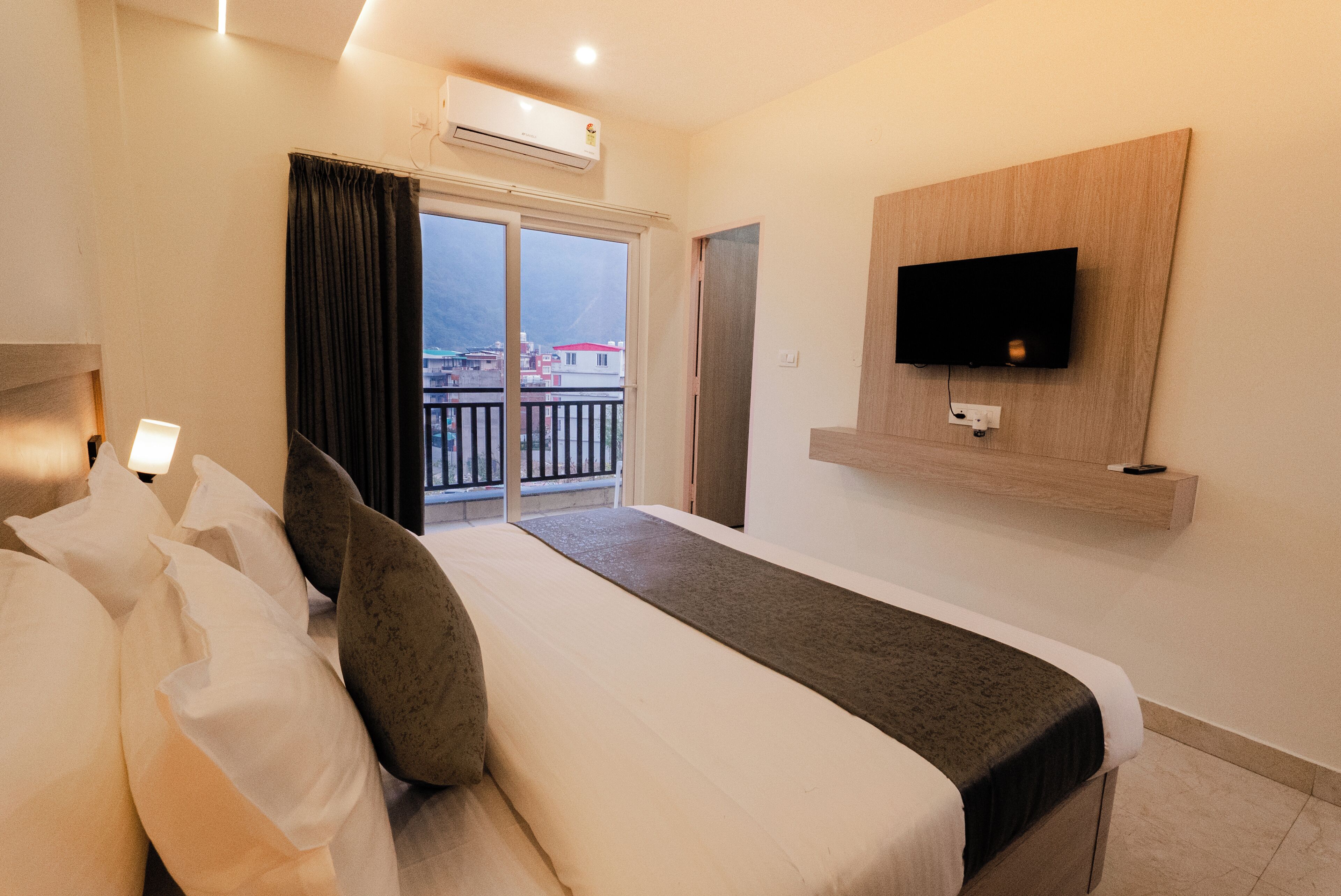 A hotel room with a bed, a TV mounted on the wall, and a balcony with a view.