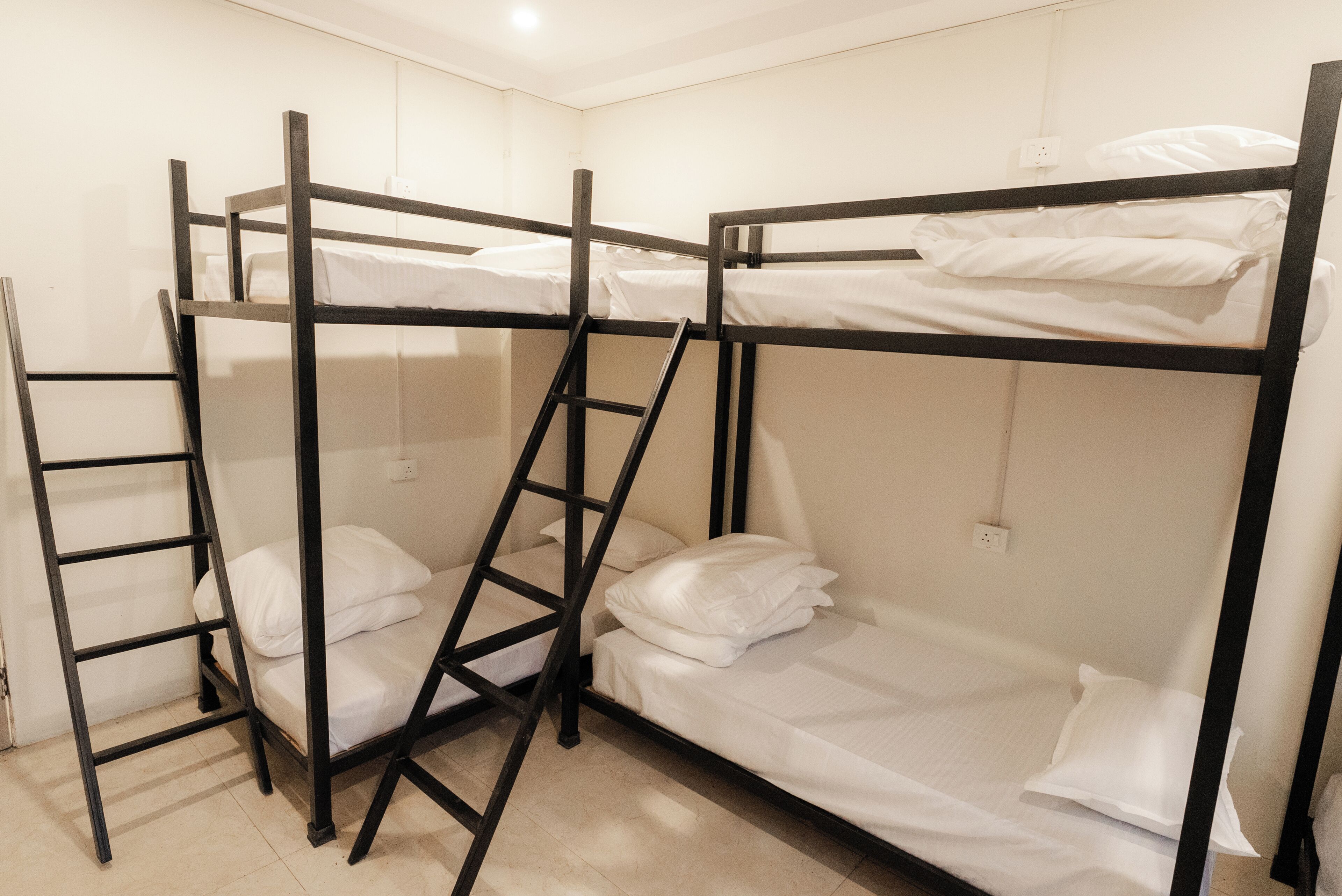 A bunk bed room with a ladder, white bedding, and a plain wall.