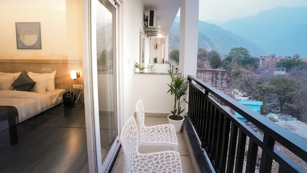 A balcony with a white chair, a potted plant, and a view of distant buildings and mountains. - Alpine Retreat (Rishikesh)