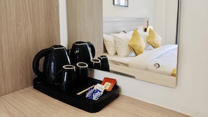 A hotel room with a wooden floor, a coffee station with black kettles, a bed with white and yellow pillows, and a framed picture on the wall. - Alpine Retreat (Rishikesh)