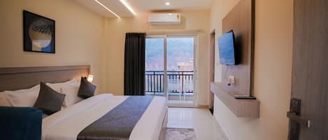 Habitación de hotel con cama, televisor, aire acondicionado, ventilador de techo y vistas al exterior.