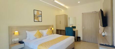 A modern hotel room with a large bed, bedside lamps, a desk with a chair, a television, and a ceiling fan.