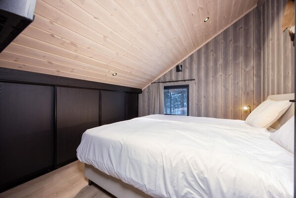 A bedroom with a sloped ceiling, a large bed, a window, and a wall-mounted light fixture. - Lakelodge 10p in Vr dal (Kviteseid)