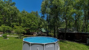 Piscina exterior con estructura metálica y revestimiento azul, rodeada de césped y árboles.