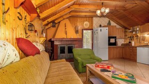 Interior acogedor de una cabaña con techo de madera, chimenea, sofá, sillón verde y una zona de cocina.