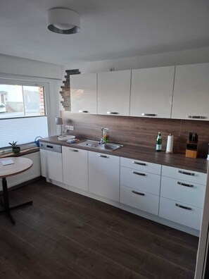 Eine moderne Küche mit weißen Schränken, einer Holz Arbeitsplatte, einem eingebauten Geschirrspüler und einem Fenster mit Jalousien.