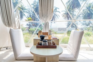 A room with a round table, two chairs, a tray with kitchen items, and a view of palm trees through large windows.
