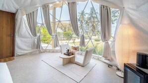 A tented room with a table, chairs, a lamp, and a TV. - Grood Glamping (Bang Saphan)
