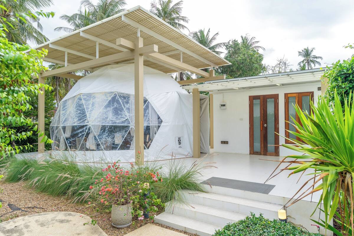 A modern house with a covered outdoor area, a large white dome structure, and a wooden door.