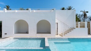 A modern pool area with a clear blue pool, white walls, and a staircase leading to an upper level. - Grood Glamping (Bang Saphan)