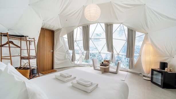 A tent-style room with a bed, a wooden chair, a small table, and a hanging light fixture. - Grood Glamping (Bang Saphan)