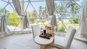 A room with a view of palm trees, a table with a tray, and a chair. - Grood Glamping (Bang Saphan)
