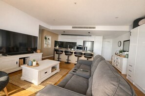 A modern living room with a grey sofa, a flat-screen TV, and a kitchen area with bar stools. - Designer 2 Bedroom Apartment in South Brisbane (South Brisbane)
