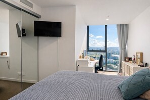 A modern bedroom with a large bed, a desk, a TV, and a city view. - Designer 2 Bedroom Apartment in South Brisbane (South Brisbane)