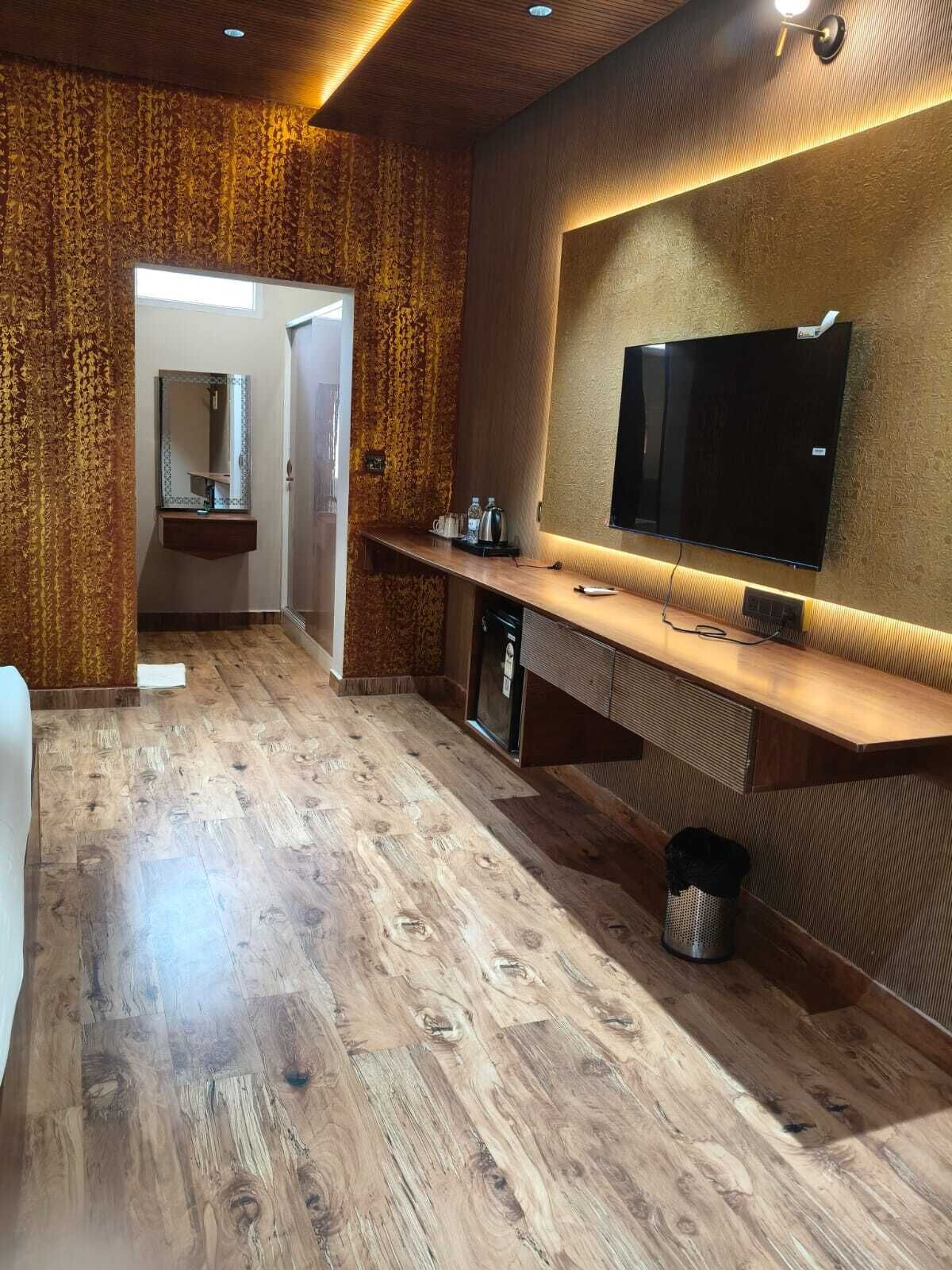 Ein modernes Badezimmer mit Holzboden, Waschbecken, Spiegel und einem an der Wand montierten Fernseher.