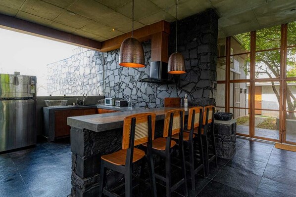 A modern kitchen with a stone backsplash, bar stools, and pendant lighting. - Meraki (Shoolagiri)