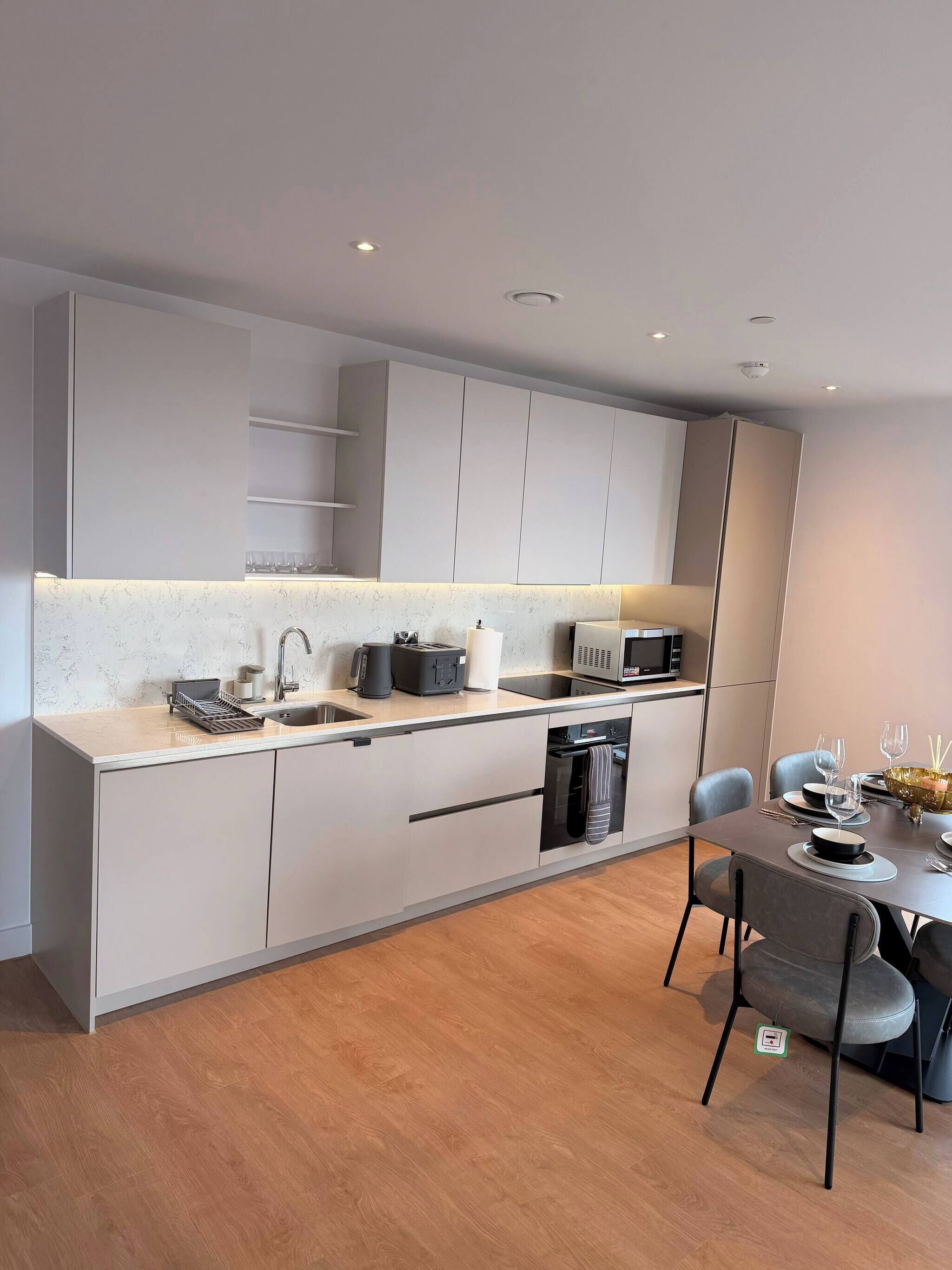 A modern kitchen with a built-in oven, microwave, and sink. There is a dining area with a table and chairs.