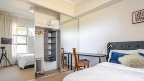 A bedroom with a bed, a desk, a chair, a radiator, and a wardrobe.