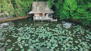 A houseboat with a thatched roof, surrounded by a pond with lily pads. - Tranquility living in the garden ,20km from airport (ฉะเชิงเทรา)