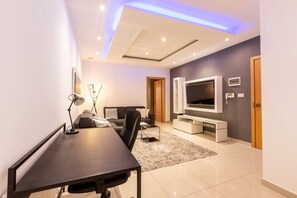 Ein modernes Wohnzimmer mit Flachbildfernseher, einer Couch, einem Esstisch und einer Decke mit eingelassenen Leuchten.