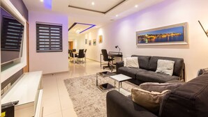 A modern living room with a flat-screen TV, a sofa, a coffee table, and a dining area with chairs and a table. - Sliema Bluemist near Balluta Bay (Sliema)