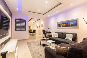 Ein modernes Wohnzimmer mit Flachbildfernseher, einer Couch, einem Couchtisch und einem Essbereich mit Stühlen und Tisch.