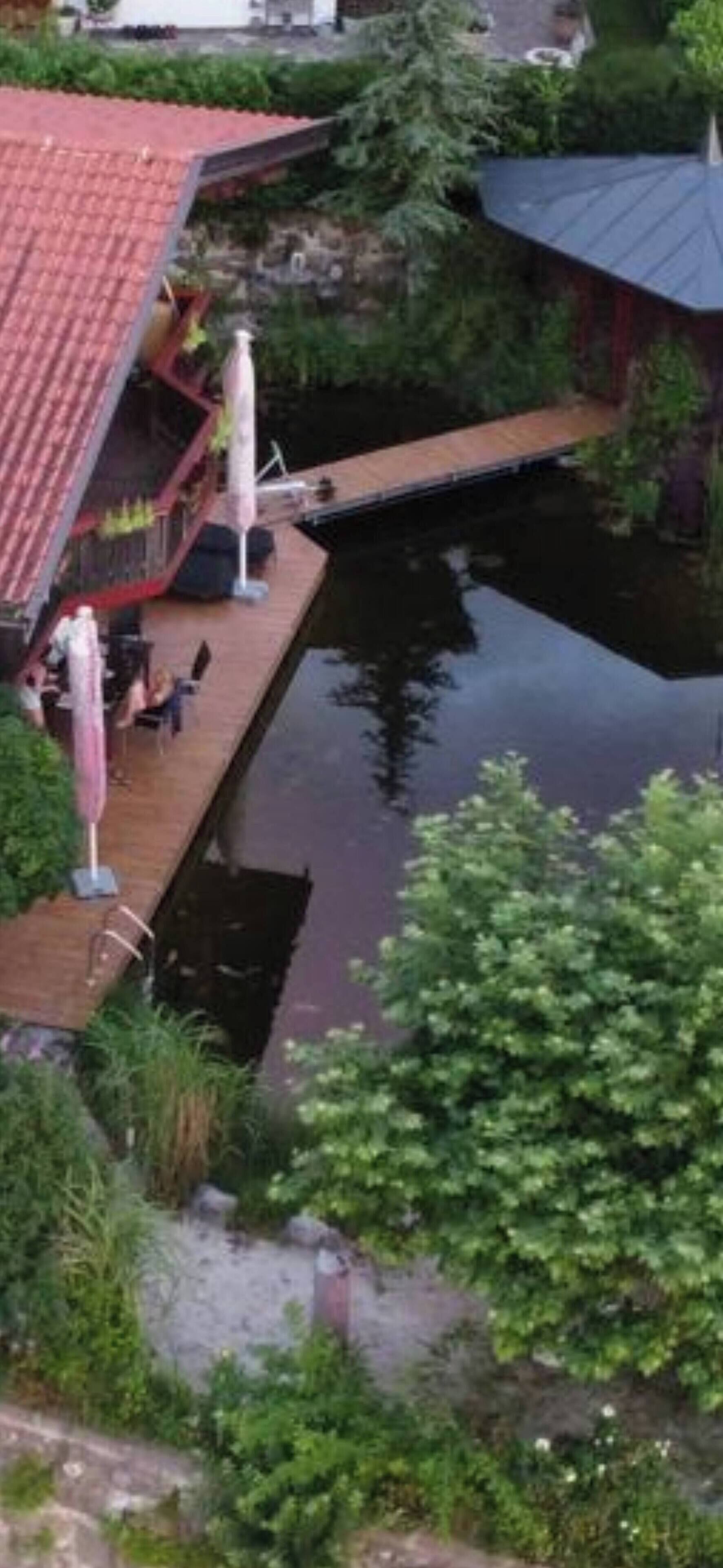 Un muelle se adentra en una masa de agua, con un edificio de techo rojo y mesas al aire libre.