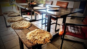 Un espace repas comprenant une table en bois, quatre bancs dotés de coussins d’assise tissés et des chaises en cuir marron.