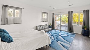 A modern hotel room with a bed, a sofa, a large window with curtains, and a view of the outdoors. - Beverly Hills Home • Guest House & Hot Tub (Beverly Hills)