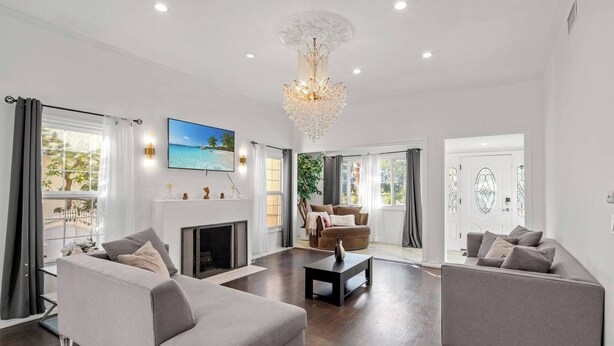 A modern living room with a fireplace, a chandelier, and a large TV. - Beverly Hills Home • Guest House & Hot Tub (Beverly Hills)