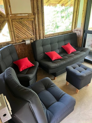 A room with a black leather sofa set, two red cushions, and a wooden floor.