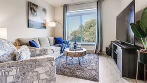 Ett modernt vardagsrum med en soffa, ett soffbord, en tv och stora fönster.