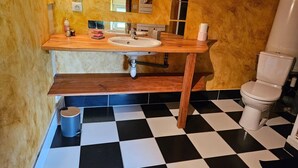 Un baño con tocador de madera, lavamanos, espejo, inodoro y suelo de cuadros.