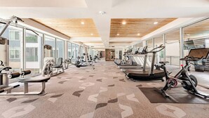Un gimnasio con equipamiento de ejercicio, ventanas amplias y una alfombra estampada.