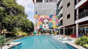 Una piscina con un mural, una advertencia de profundidad de 1.2 metros y un edificio con balcones.