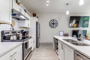 Una cocina moderna con armarios blancos, electrodomésticos de acero inoxidable, un reloj y un televisor de pantalla plana.