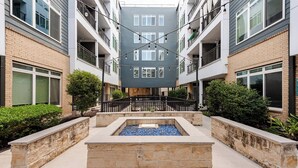 Un edificio residencial de varios pisos con balcones, un patio central con fuente de agua y un muro de contención de piedra.