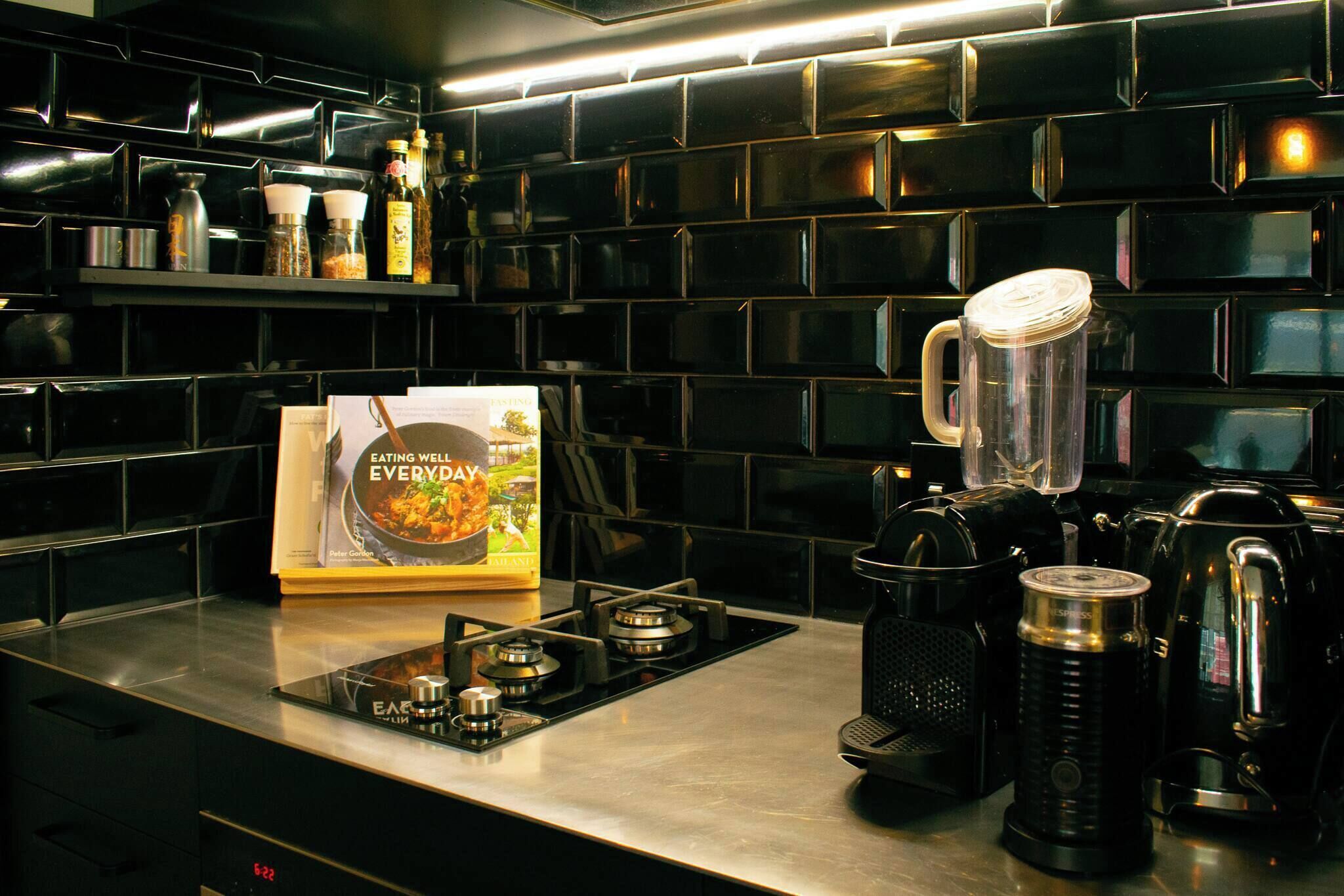 Eine Küche mit schwarzem Fliesenrückwand, einem Gasherd, einer Kaffeemaschine und einem Kochbuch mit dem Titel 'Eating Well Everyday' auf der Arbeitsfläche.