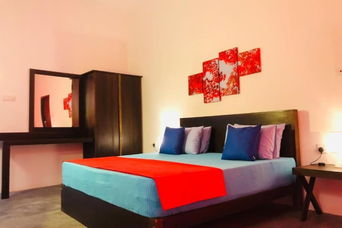 A bedroom with a bed, a nightstand, a mirror, and a red artwork on the wall.