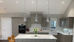 Una cocina moderna con armarios grises, una isla central, iluminación colgante y un horno empotrado.