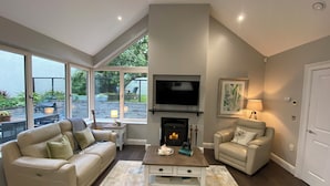 Un salón con chimenea, televisor y ventana grande con vistas a un jardín.